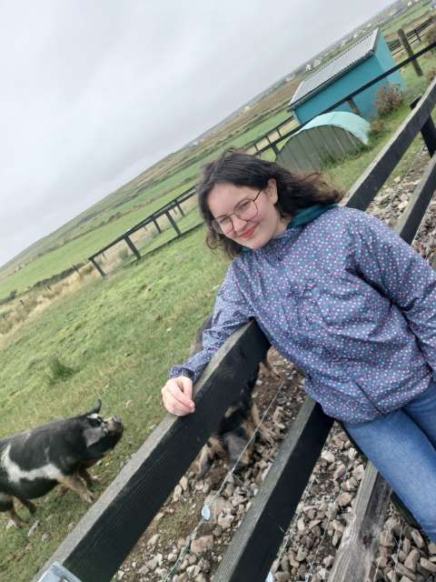 Ella leaning on a fence beside a pig