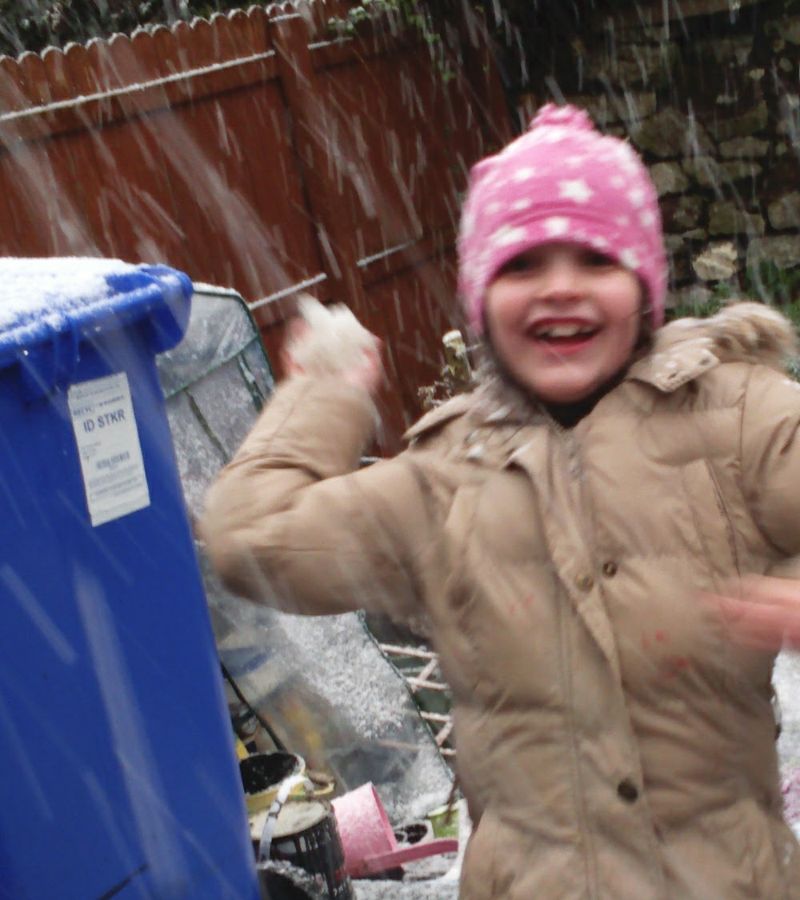 Young Ella laughing in the snow in a pink hat