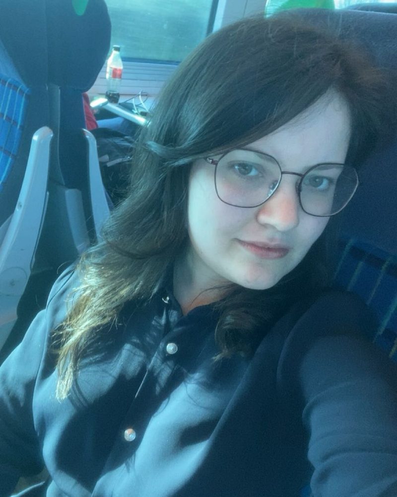 Ella in a dark shirt on a train